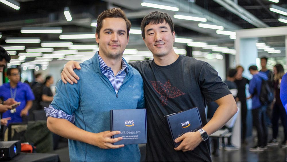 Tech innovators at a hackathon proudly display their AWS DeepLens rewards, celebrating achievement and collaboration in machine learning development.