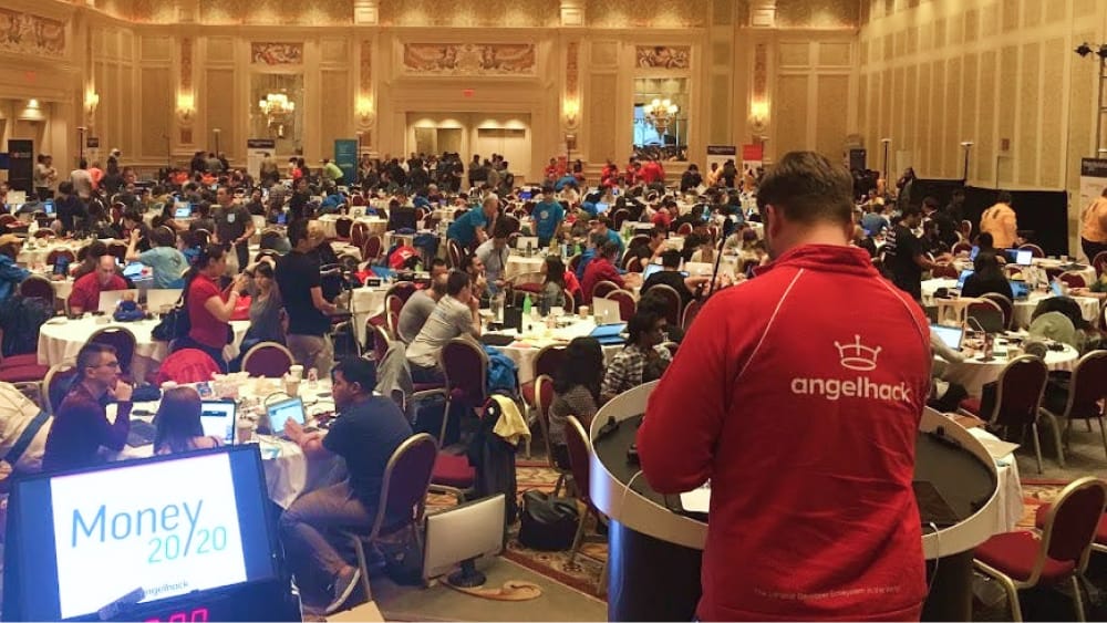 A person wearing a red t-shirt with the AngelHack logo addressing a crowd.